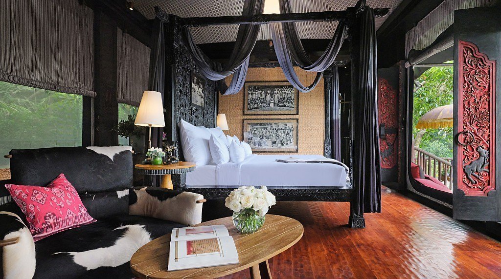 Canopy bed and lounge with carved red doors open to the jungle at Capella Ubud