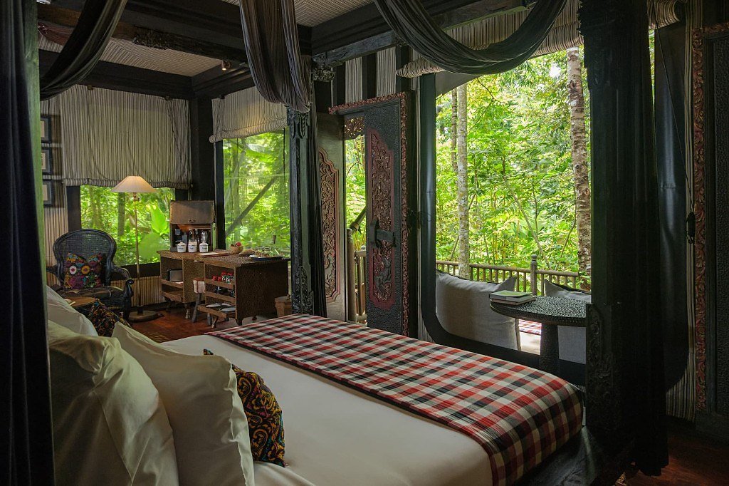 Four-poster bed and carved doors opening to the jungle in a tent suite at Capella Ubud